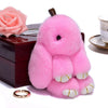 A fluffy pink angel bunny keychain with a pom pom tail resting on a dark box.