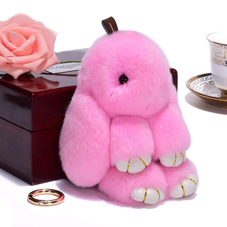 A fluffy pink angel bunny keychain with a pom pom tail resting on a dark box.