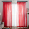 Red sheer voile curtains with a white spherical light fixture hanging above a window.