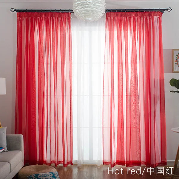 Red sheer voile curtains with a white spherical light fixture hanging above a window.