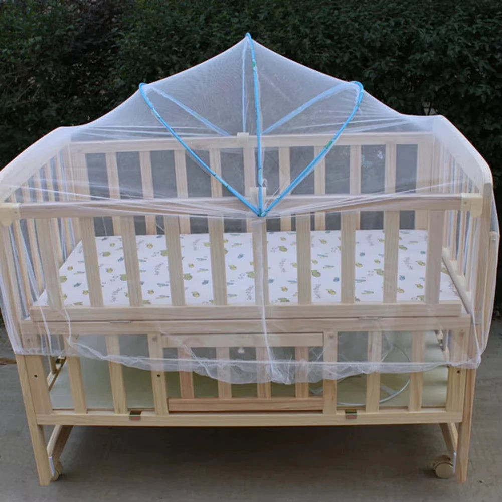 A wooden baby crib covered with a sheer, breathable mosquito net for protection.