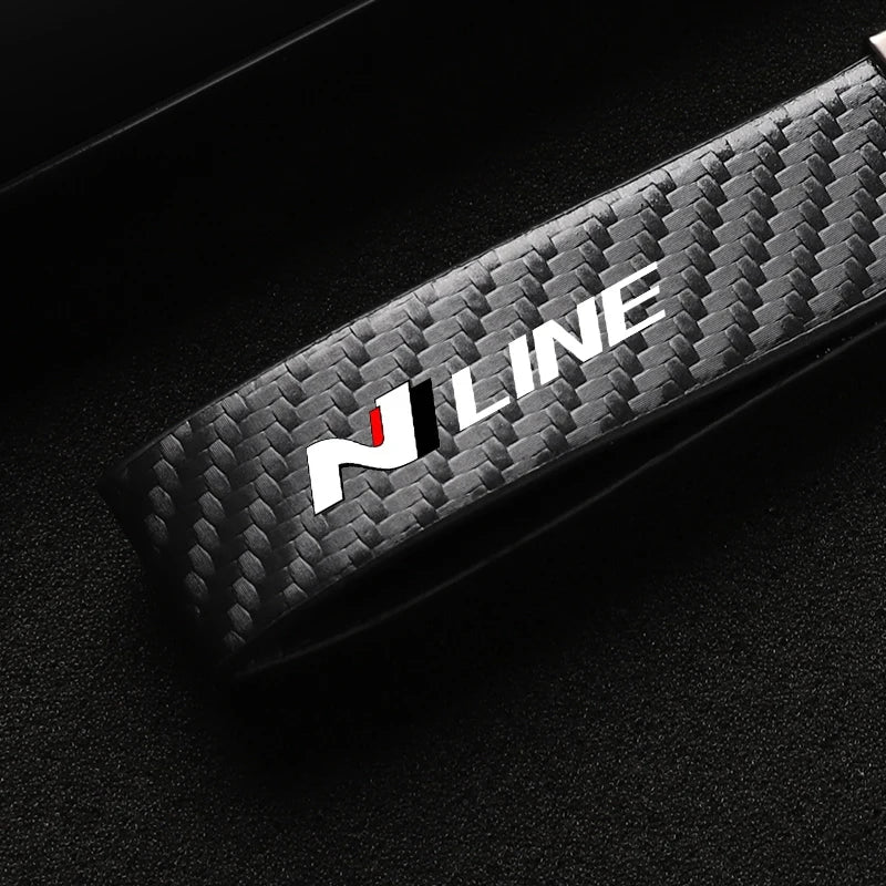 A close-up shot of a black carbon fiber style leather keychain with an N LINE logo and swivel buckle.