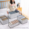 A person is organizing folded clothing in various gray storage boxes on a white bed.