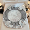A round, ruffled faux fur fitted sheet and pillowcase set in gray and white tones.
