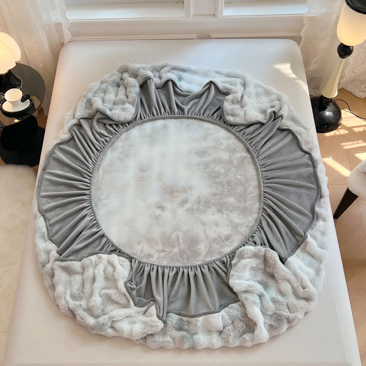 A round, ruffled faux fur fitted sheet and pillowcase set in gray and white tones.