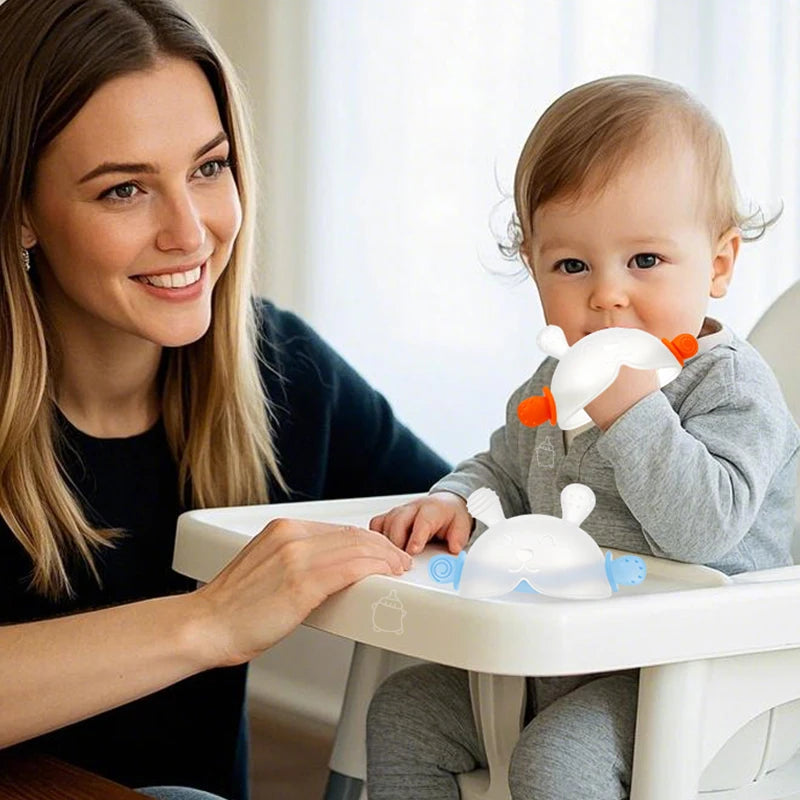 A woman is holding a bunny-shaped silicone baby teether for a baby in a high chair.