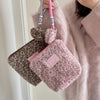 A pink faux fur cosmetic bag with a leopard print fabric is hanging from a strap against a light pink sweater.