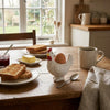 A rustic breakfast setting featuring a ceramic chicken egg cup, sliced toast, and a cup of coffee on a wooden table.