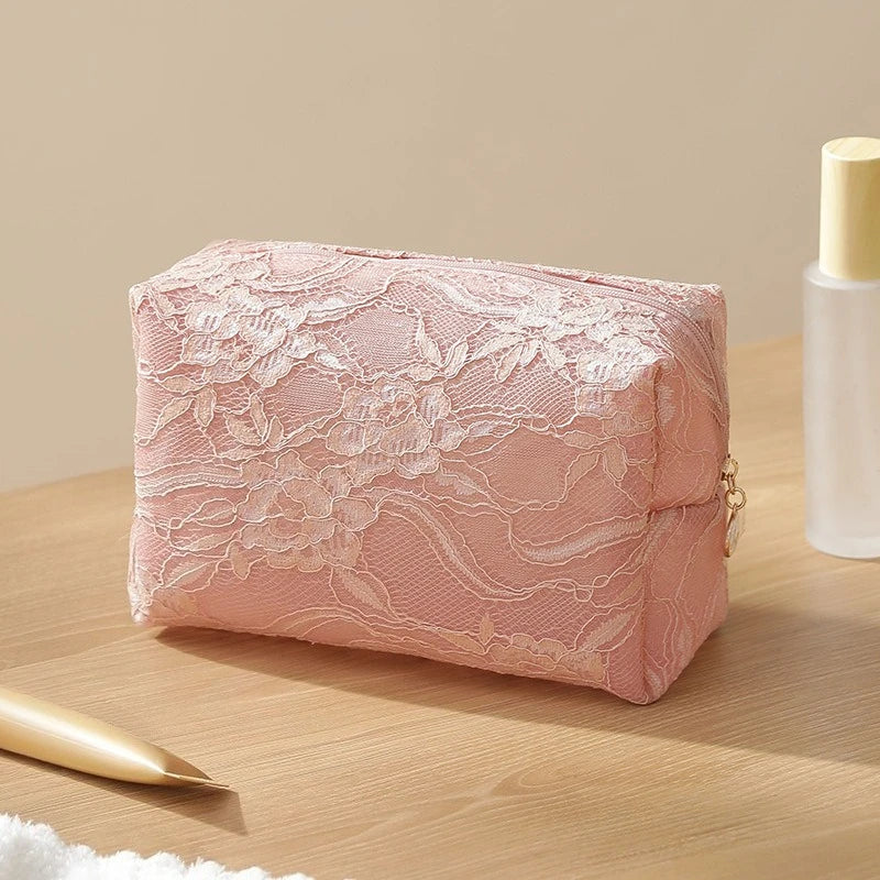 A pink lace mesh makeup bag resting on a wooden surface next to a glass bottle.