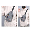 A light beige canvas crossbody chest bag with black straps shown on a person's torso.
