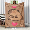 A tan flannel throw blanket featuring a cartoon capybara design with pink hearts, displayed on a wooden bed frame.