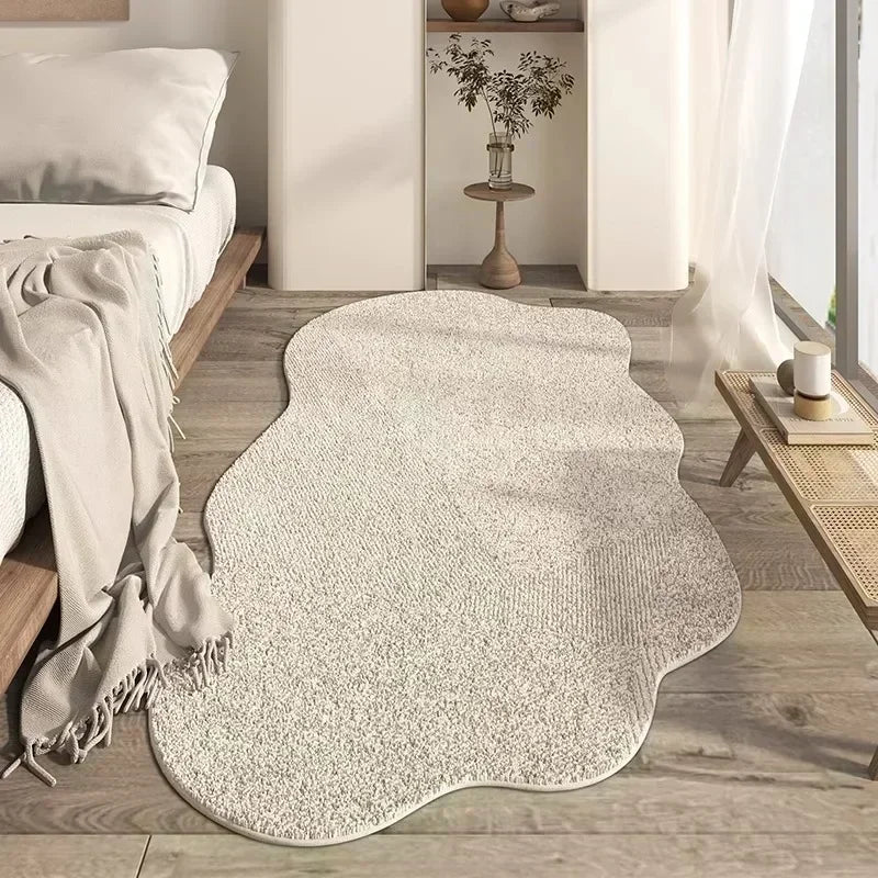 A light beige irregular area rug with a plush texture placed on a wooden floor next to a white sofa and sheer curtains.