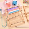 A wooden weaving loom kit with colorful yarn and threads is displayed on a light pink background.