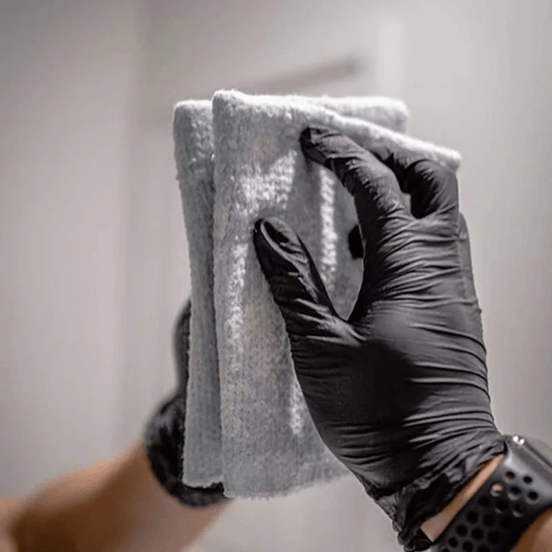 A hand wearing a black nitrile glove is holding and wiping a gray towel.