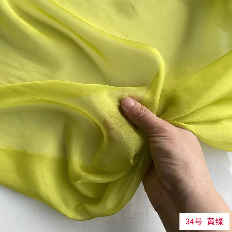 A hand is gently folding a piece of bright lime green sheer silk chiffon fabric.