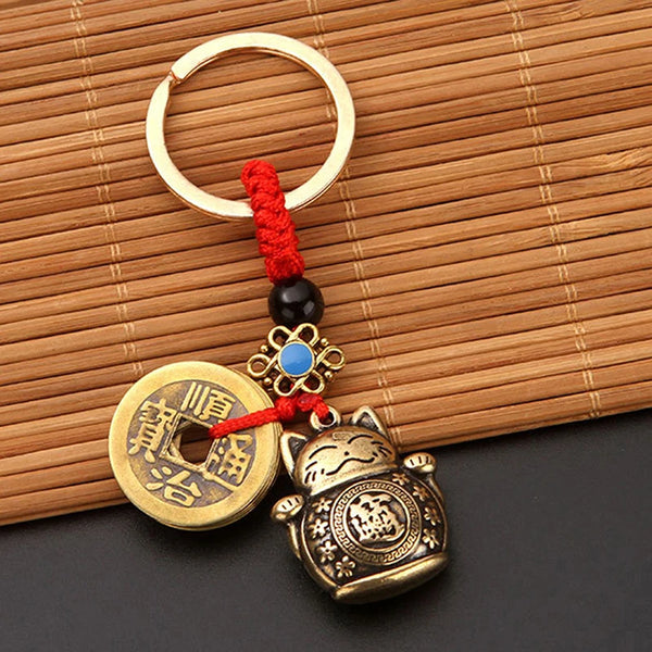 Vintage lucky cat keychain featuring a coin design and red tassel attached to a gold ring.