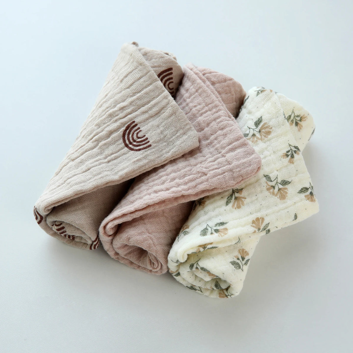 A stack of soft, natural colored cotton gauze burp cloths for babies.