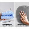 A hand holds a blue silicone shower scrubber pad, showing its texture and use for cleaning or massage.