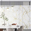 Modern dining room featuring a white marble table and chairs against a wall with gold veined marble peel-and-stick panels.