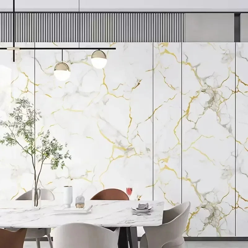 Modern dining room featuring a white marble table and chairs against a wall with gold veined marble peel-and-stick panels.