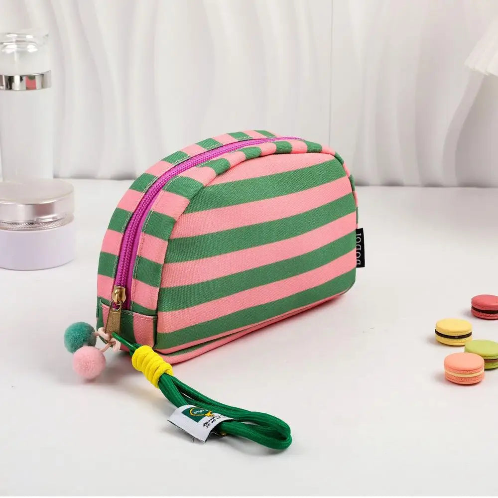 Pochette en crochet rayée rose et vert avec pompon jaune, exposée sur une surface blanche.