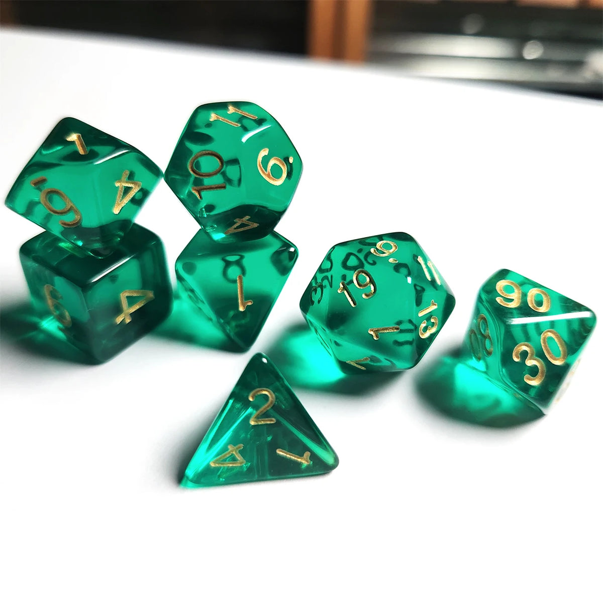 A set of seven translucent green acrylic polyhedral dice resting on a white surface.