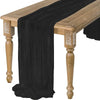 A dark black cotton gauze table runner draped over a rustic wooden table.
