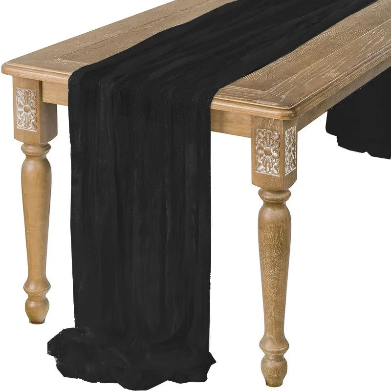 A dark black cotton gauze table runner draped over a rustic wooden table.