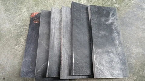 A stack of black buffalo horn knife handle scales, showing various textures and finishes.