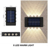 A black solar powered wall light with an upper solar panel and eight warm LED lights illuminating a textured wall.