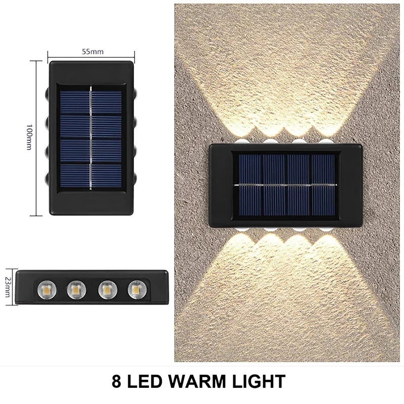A black solar powered wall light with an upper solar panel and eight warm LED lights illuminating a textured wall.