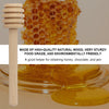A wooden honey dipper stick next to golden honey and jam on a glass dish.