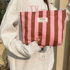 A person holds a striped canvas cosmetic bag with pink and brown stripes against a light gray sweatshirt.