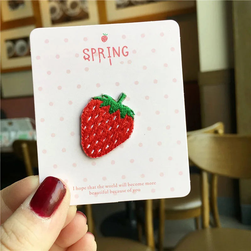 A pink card featuring a red strawberry 3D embroidery patch with the word SPRING on it.