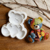 A colorful crochet texture teddy bear is lying next to a white silicone mold shaped like a bear for crafting.