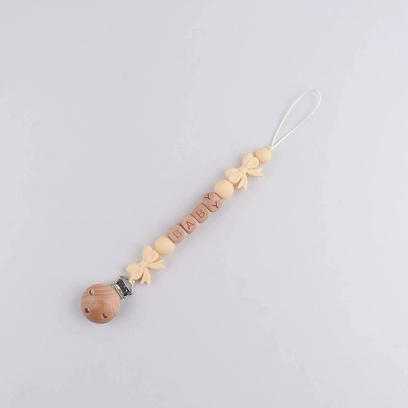 A string of wooden beads and fabric flowers with the name BABY and a silicone clip on a white background.