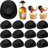 Black miniature cowboy hats for party favors and cake toppers displayed next to a bottle of liquor and cupcakes.