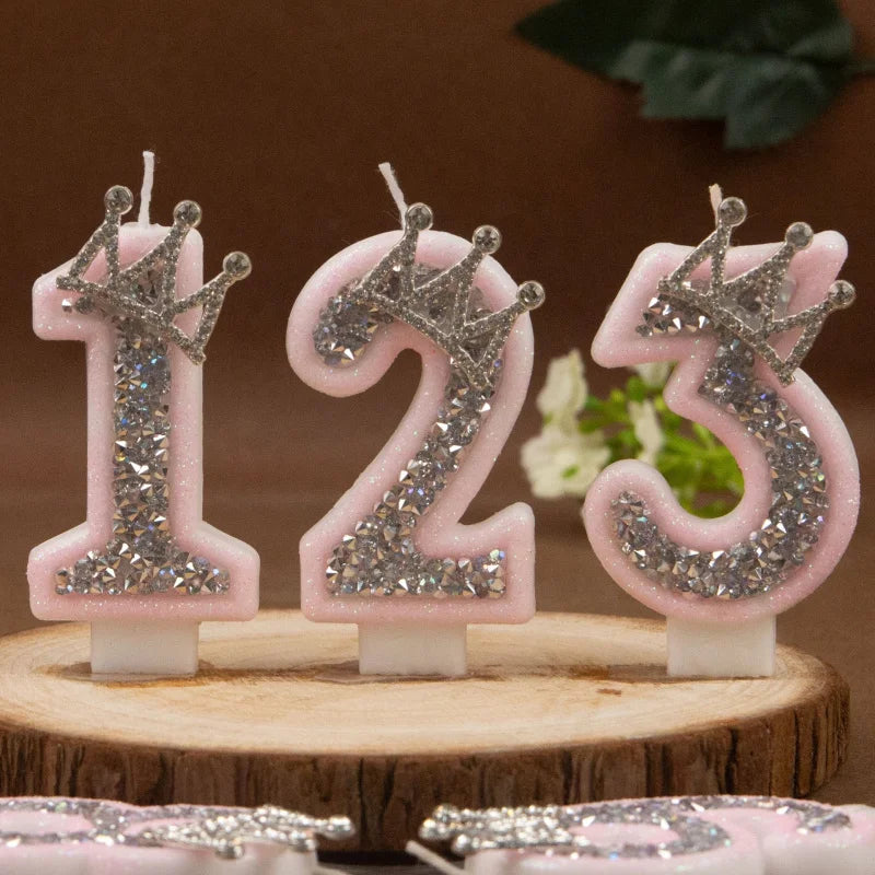 Three pink rhinestone crown number candles spelling out 123 displayed on a wooden surface.