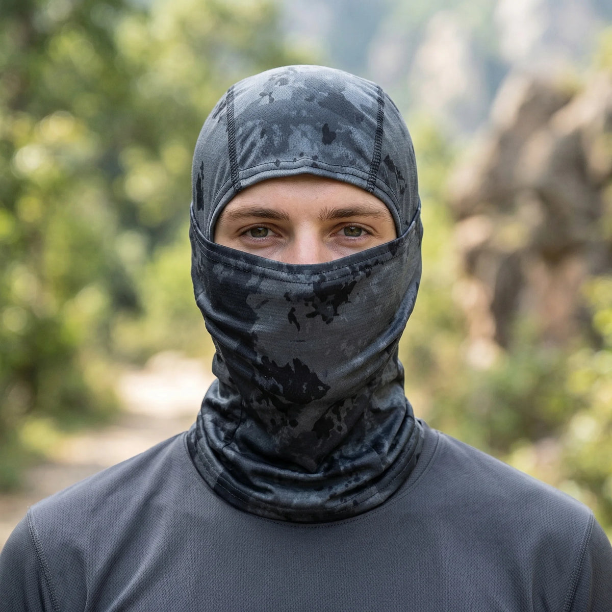 A man wearing a dark gray stretchy breathable balaclava cap in an outdoor setting.