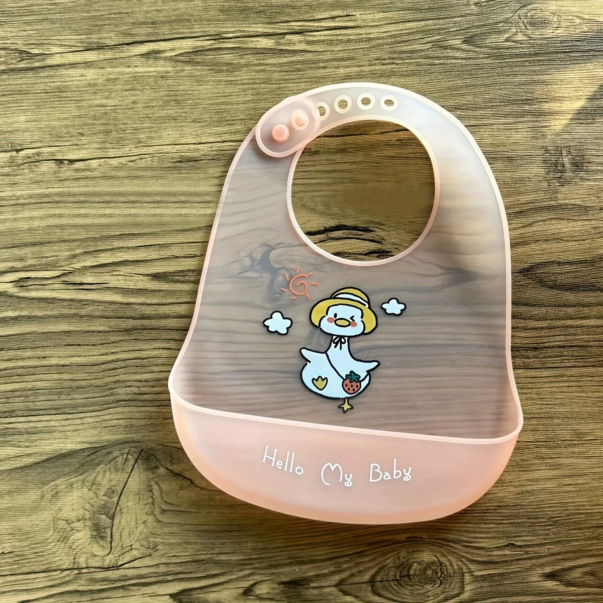 A pink silicone baby bib with a cartoon duck design resting on a wooden surface.