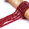 A strand of faceted red crystal glass spacer beads is draped over a gold-colored cylindrical object.