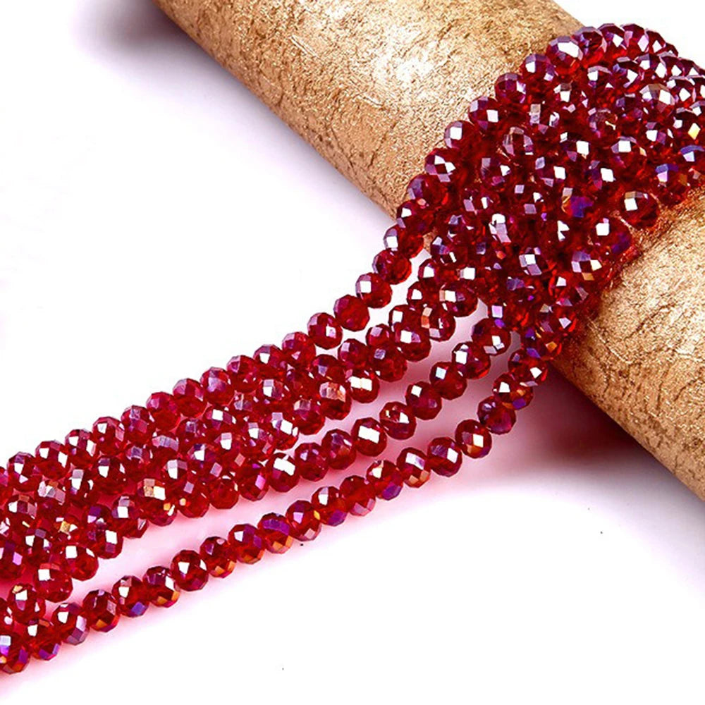 A strand of faceted red crystal glass spacer beads is draped over a gold-colored cylindrical object.