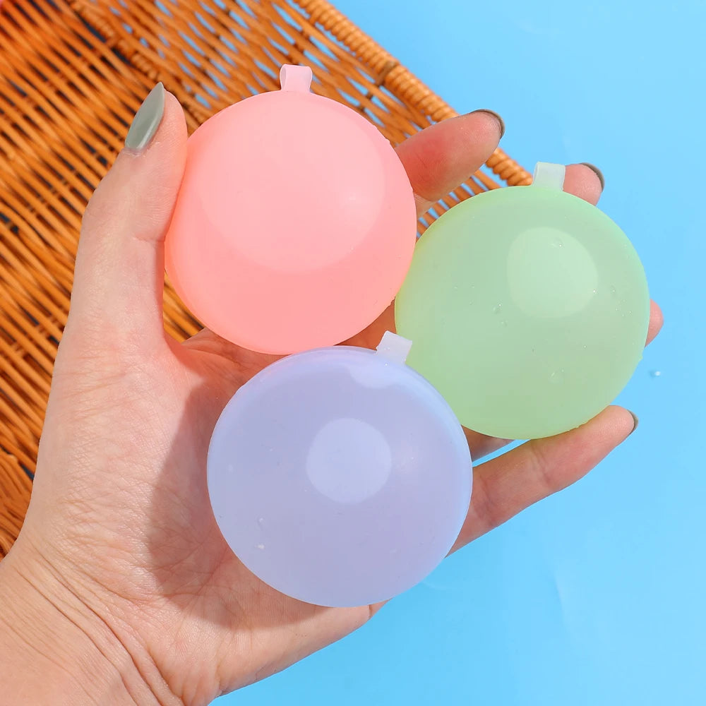 Eine Hand hält drei wiederverwendbare Silikon-Wasserballons in rosa, hellgrün und lavendelfarben vor blauem Hintergrund.