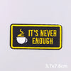 Black embroidered iron-on patch with yellow text saying It's never enough and a steaming cup icon