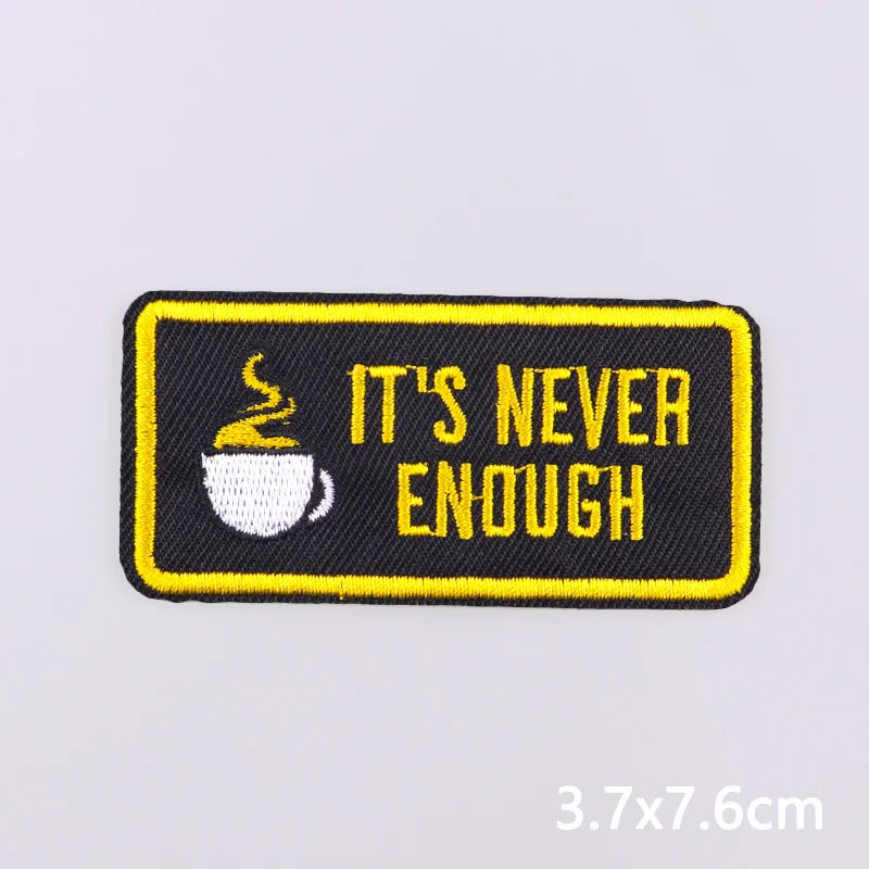 Black embroidered iron-on patch with yellow text saying It's never enough and a steaming cup icon