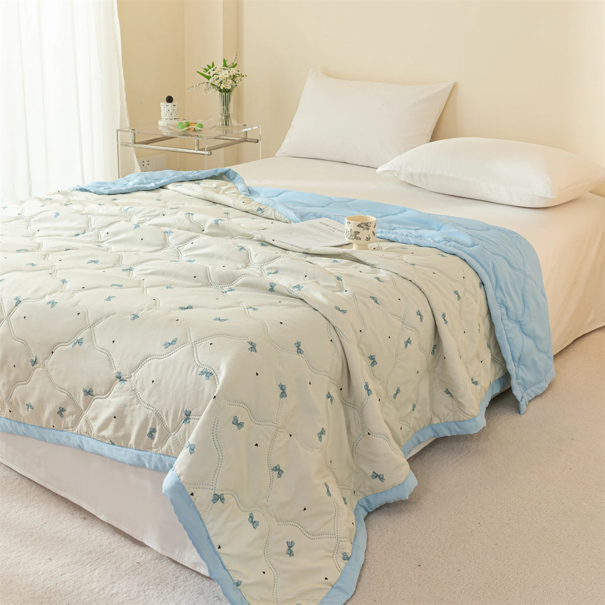 A light blue and white quilted summer quilt is displayed on a bed with white linens.