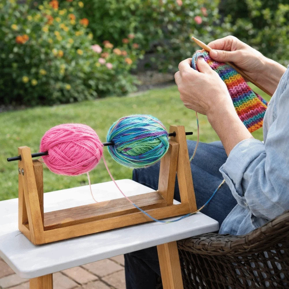 Hands are spinning a colorful yarn ball on a wooden holder outdoors.