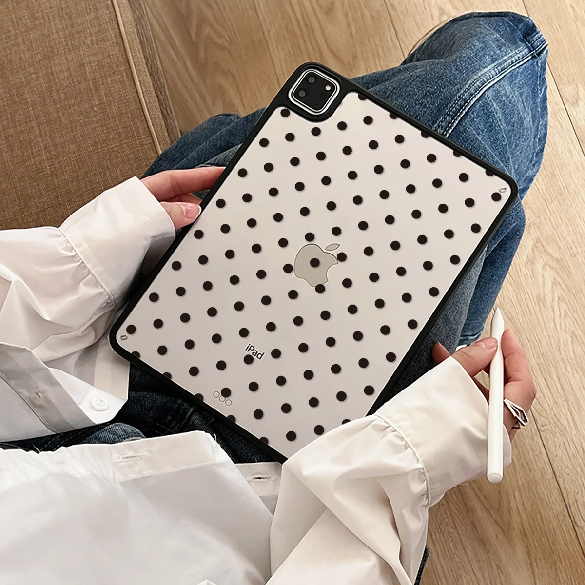 A hand holds a white iPad in a black polka dot protective case, resting on denim jeans.