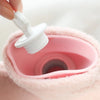 A hand is holding a white stopper from a pink plush-covered hot water bottle.