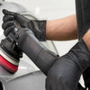 A hand wearing black nitrile gloves is using a power tool on a car surface.